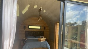 Een gezellige slaapkamer met een houten plafond, een bed met een blauwe sprei, een rieten mand en een geometrisch vloerkleed.