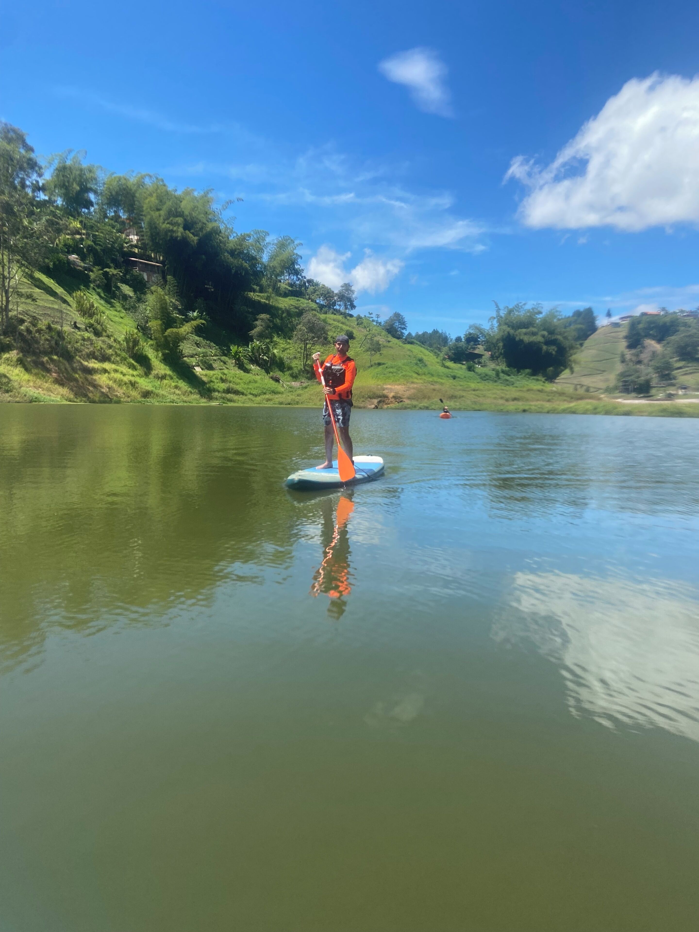 A person paddleboarding on a calm lake with lush greenery and hills in the background.