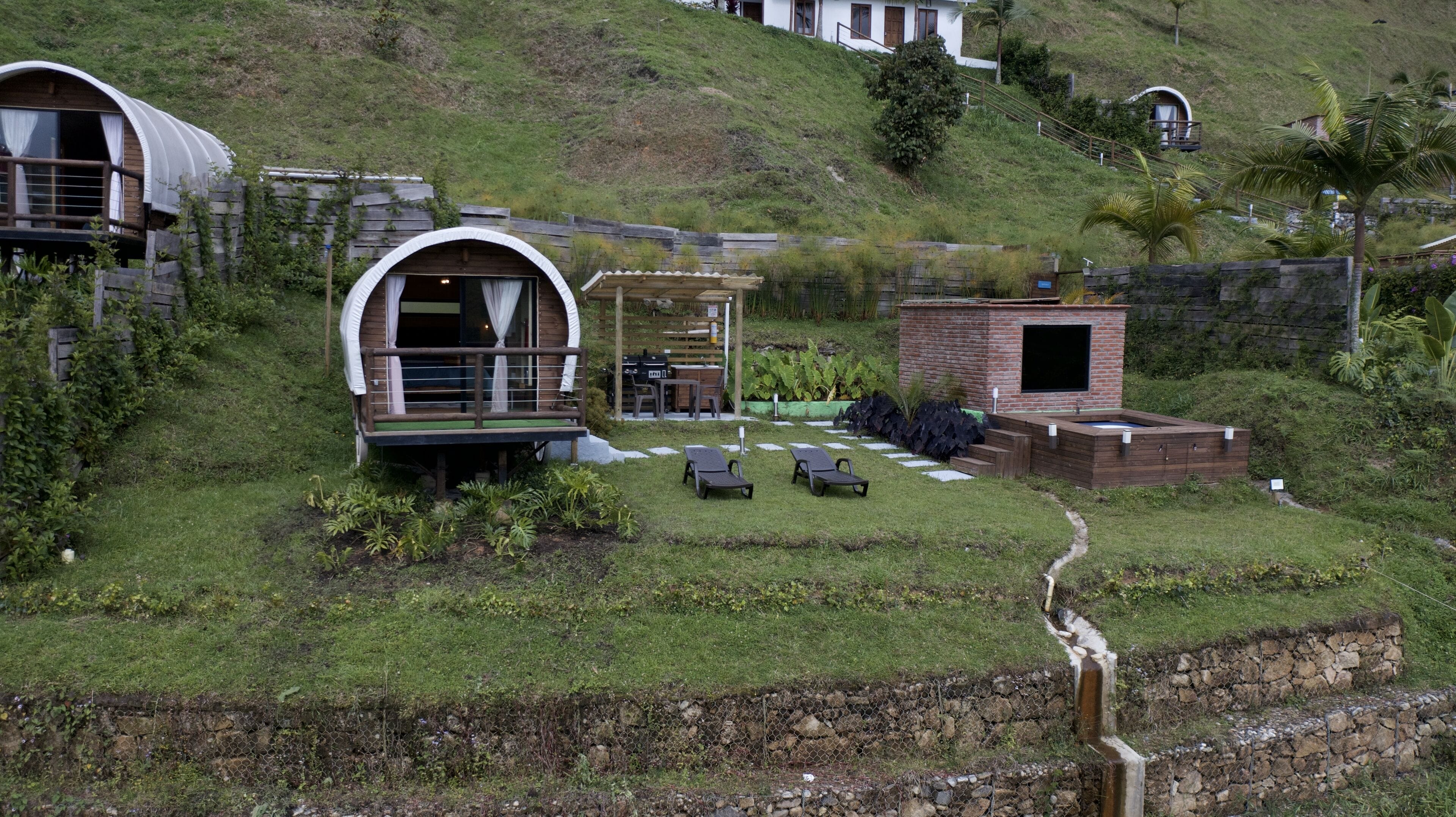 A hillside property with a covered outdoor seating area, a small brick structure, and a pool.