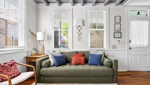 A cozy living room with a green sofa, a wooden chair, and a small table with a lamp. - Historic Downtown Home - Luxury Stay On St Philip (Charleston)