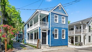 A two-story house with a front porch and a balcony, located on a street with other houses. - Historic Downtown Home - Luxury Stay On St Philip (Charleston)