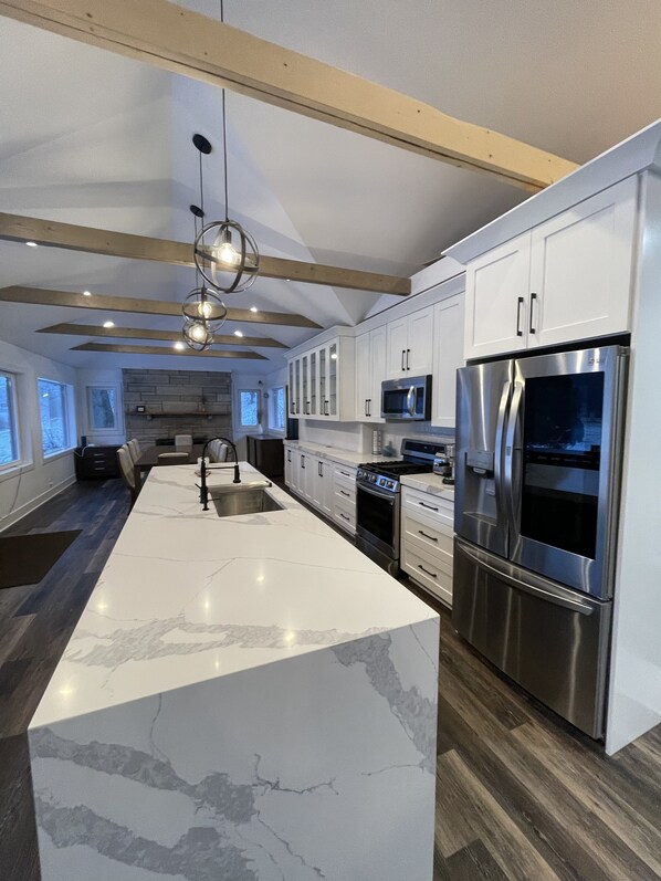 Una cocina moderna con armarios blancos, una isla grande, electrodomésticos de acero inoxidable y una viga de techo de madera.