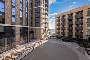 En gårdsplads med udendørs siddepladser, omgivet af høje bygninger med altaner og store vinduer.