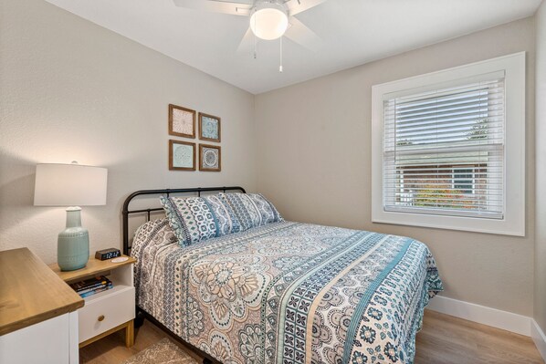 A bedroom with a bed, bedside table, lamp, and window with blinds. - Wright On Time: Central Location | Dogs Welcome (Kill Devil Hills)