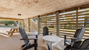 Une terrasse extérieure couverte, dotée de fauteuils Adirondack et d’une table de pique-nique, avec des lambris en bois au plafond et une vue sur les environs.