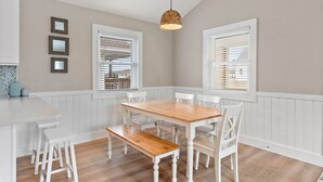 Un espace repas avec une table en bois et des chaises blanches, des murs recouverts de panneaux blancs et un luminaire suspendu.