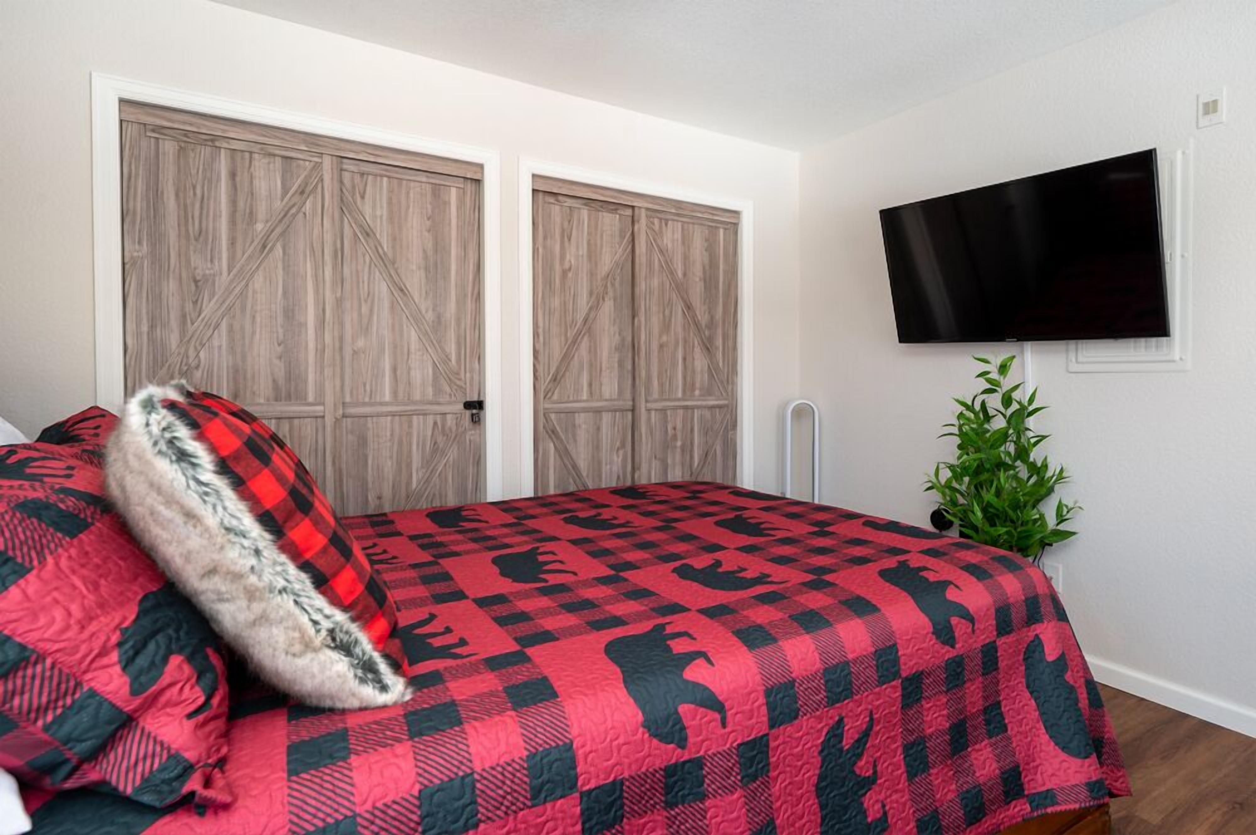 A bedroom with a checkered bedspread, two wooden doors, a television on the wall, and a small plant.