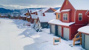A row of red wooden houses with snow-covered roofs and a clear view of mountains in the background. - Waterside West A303 Ideal and modern 1 bedroom - open floor plan and mt views (Fraser)