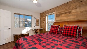A bedroom with a large bed, wooden walls, and a window with a view of snow-covered mountains. - Waterside West A303 Ideal and modern 1 bedroom - open floor plan and mt views (Fraser)