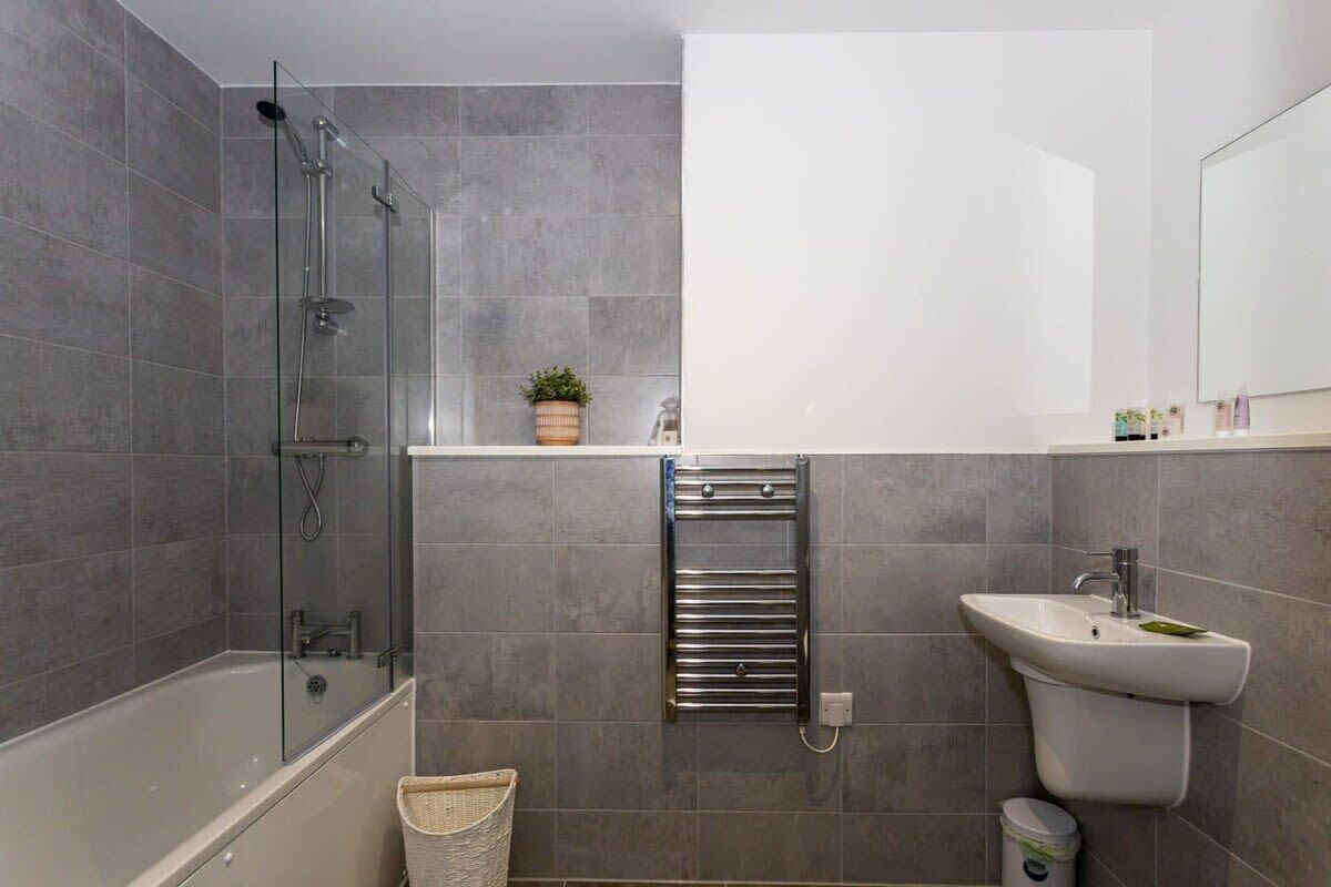A modern bathroom with a glass-enclosed shower, a white sink, and a towel rack.