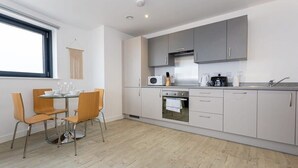 Une cuisine moderne avec des meubles gris, une hotte en acier inoxydable et un coin repas comprenant deux chaises orange et une table ronde.