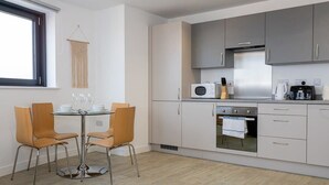 Une cuisine moderne avec des armoires grises, une cuisinière en acier inoxydable et un four à micro-ondes. On y trouve une table à manger avec quatre chaises et une décoration murale en macramé suspendue.