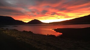 Een zonsondergang boven een meer, met bergen op de achtergrond.
