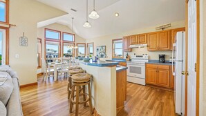 A spacious kitchen with wooden cabinets, a central island with stools, and a view of the ocean through large windows. - Canalfront Home with Private Pool, Hot Tub, Private Boat Dock, Game Room (Frisco)