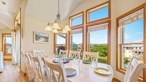 A dining area with a large table, white chairs, and a view of buildings and trees through large windows. - Canalfront Home with Private Pool, Hot Tub, Private Boat Dock, Game Room (Frisco)