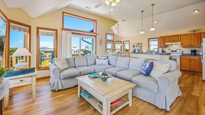 A spacious living room with a sectional sofa, wooden flooring, and large windows offering a view of the outside. - Canalfront Home with Private Pool, Hot Tub, Private Boat Dock, Game Room (Frisco)