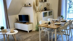 A modern living room with a flat-screen TV, white furniture, and a dining area with a wooden table and chairs. - The roofs of Nazado (2/4 people) (Erquy)
