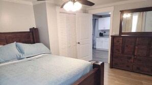 Une chambre avec un lit en bois, un ventilateur de plafond et une vue sur la cuisine.