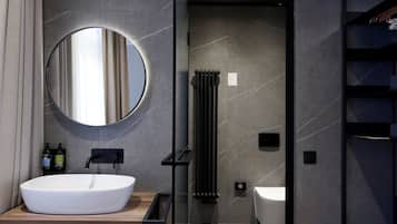 Un baño moderno con un espejo redondo, un lavamanos blanco y una bañera negra.