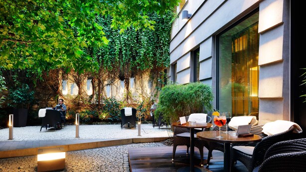 Un espace extérieur aménagé en terrasse, avec des meubles en osier, une table sur laquelle se trouve un ordinateur portable et un verre contenant une boisson.
