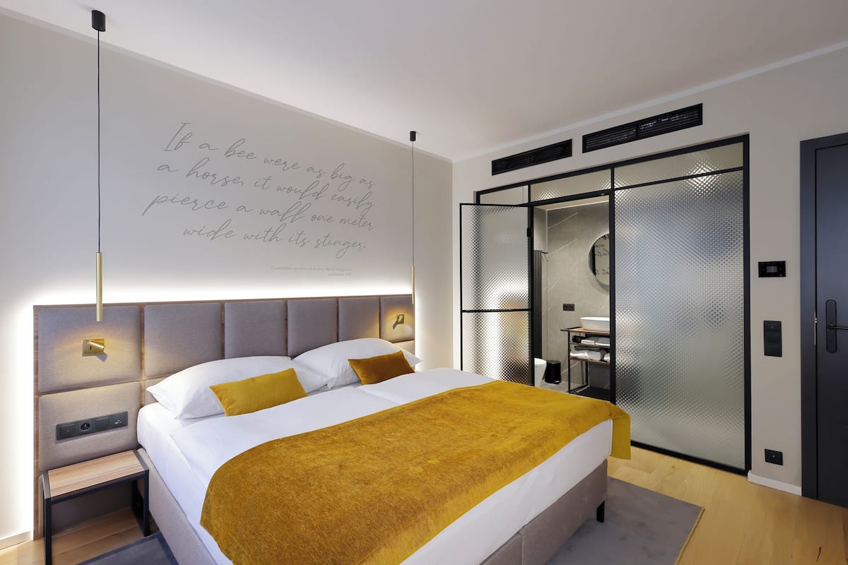 A modern bedroom with a large bed, a nightstand, a wall-mounted light, and a wardrobe with a mirrored closet door.