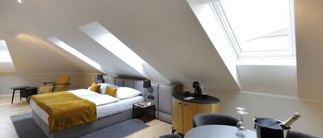 A modern hotel room with a bed, a small desk, a chair, a table, and a window.