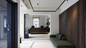 Un intérieur moderne avec un canapé, un mur en lambris de bois et un coin cuisine à l’arrière-plan.