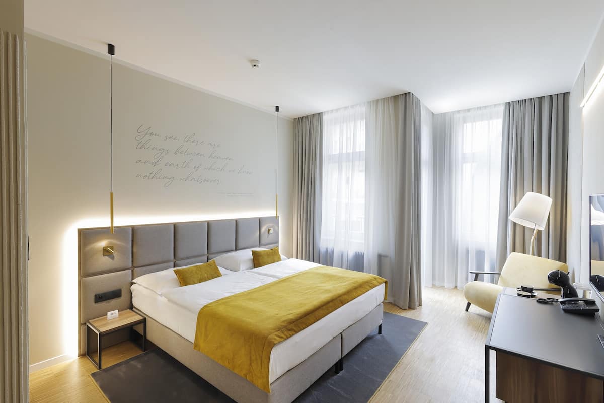 A modern hotel room with a large bed, bedside tables, a desk, and a chair.