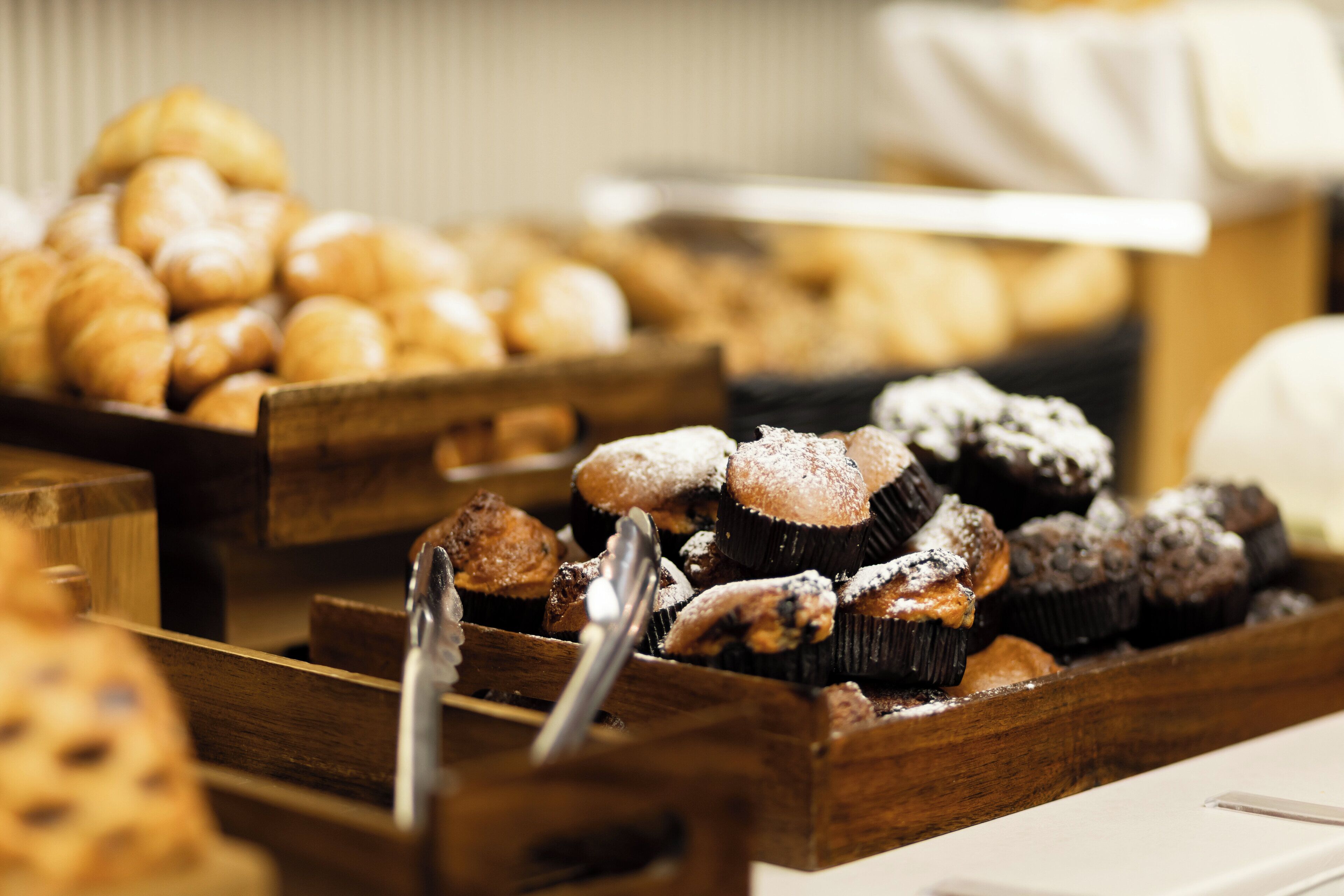 A variety of baked goods in wooden trays, including muffins and pastries.