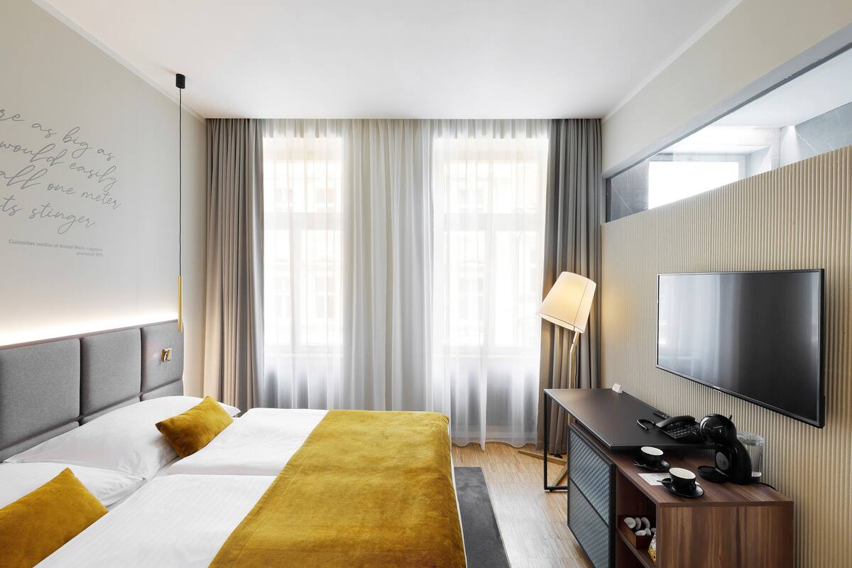 A modern hotel room with a large bed, a desk with a flat-screen TV, and a large window with curtains.