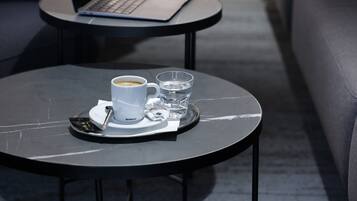 Ein moderner Außenbereich mit Sitzgelegenheit, einem Laptop, einer Tasse Kaffee und einem Glas Wasser auf einem Tisch.