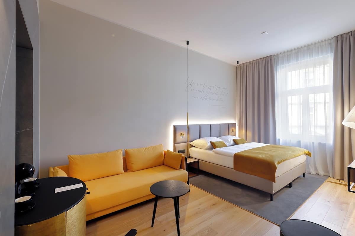 A modern hotel room with a sofa, a bed, a small table, and a wall-mounted light fixture.