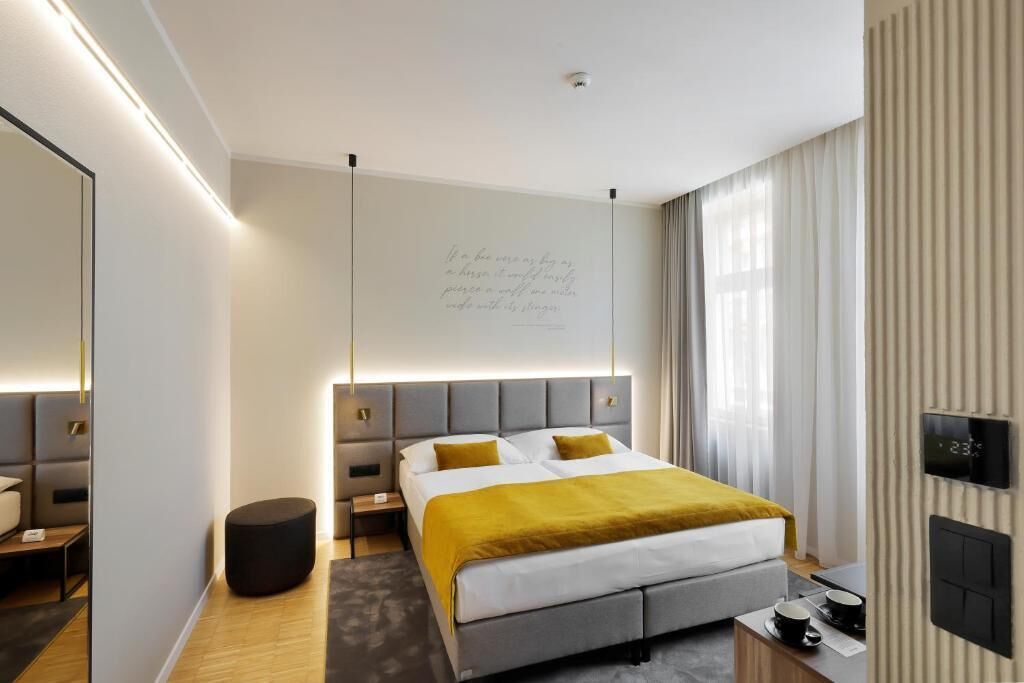 A modern hotel room with a large bed, bedside tables, a mirror, and a wall-mounted TV.
