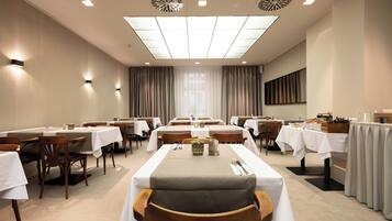 A hotel dining room with multiple tables, chairs, and a large window with curtains.