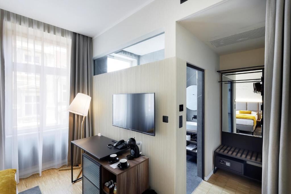 Una habitación de hotel moderna con una televisión de pantalla plana, un escritorio con teléfono y cafetera, un espejo y un armario.