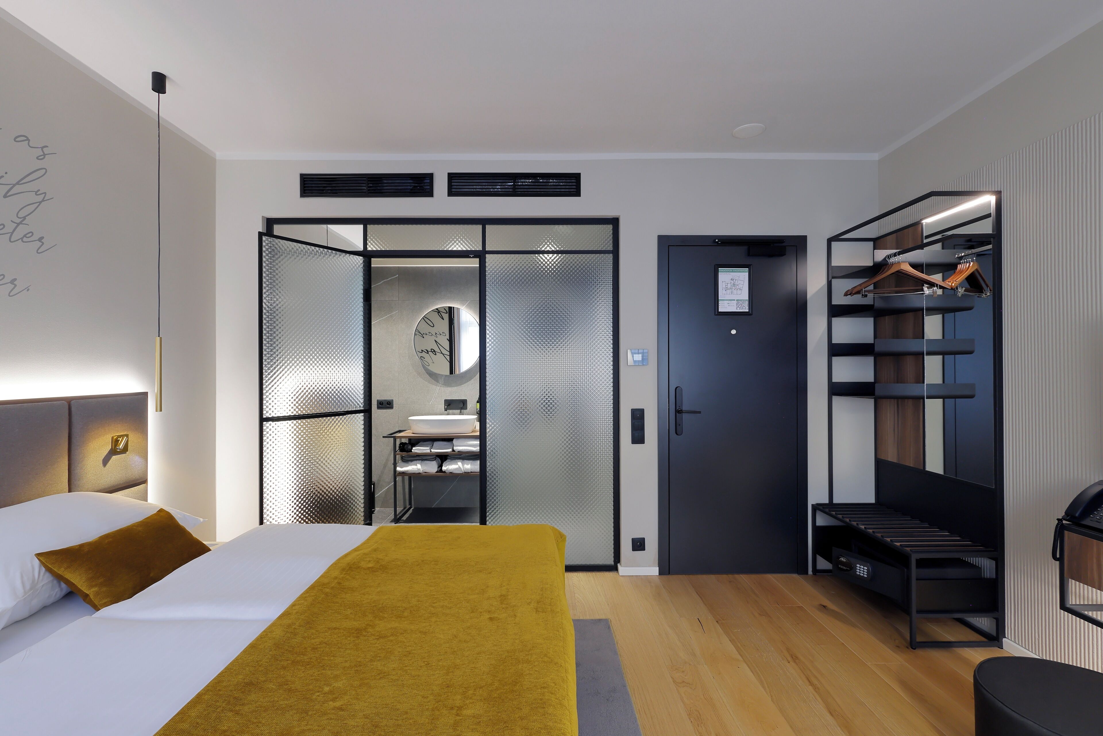 Una habitación de hotel moderna con cama, armario, espejo y estante empotrado con ropa colgada.