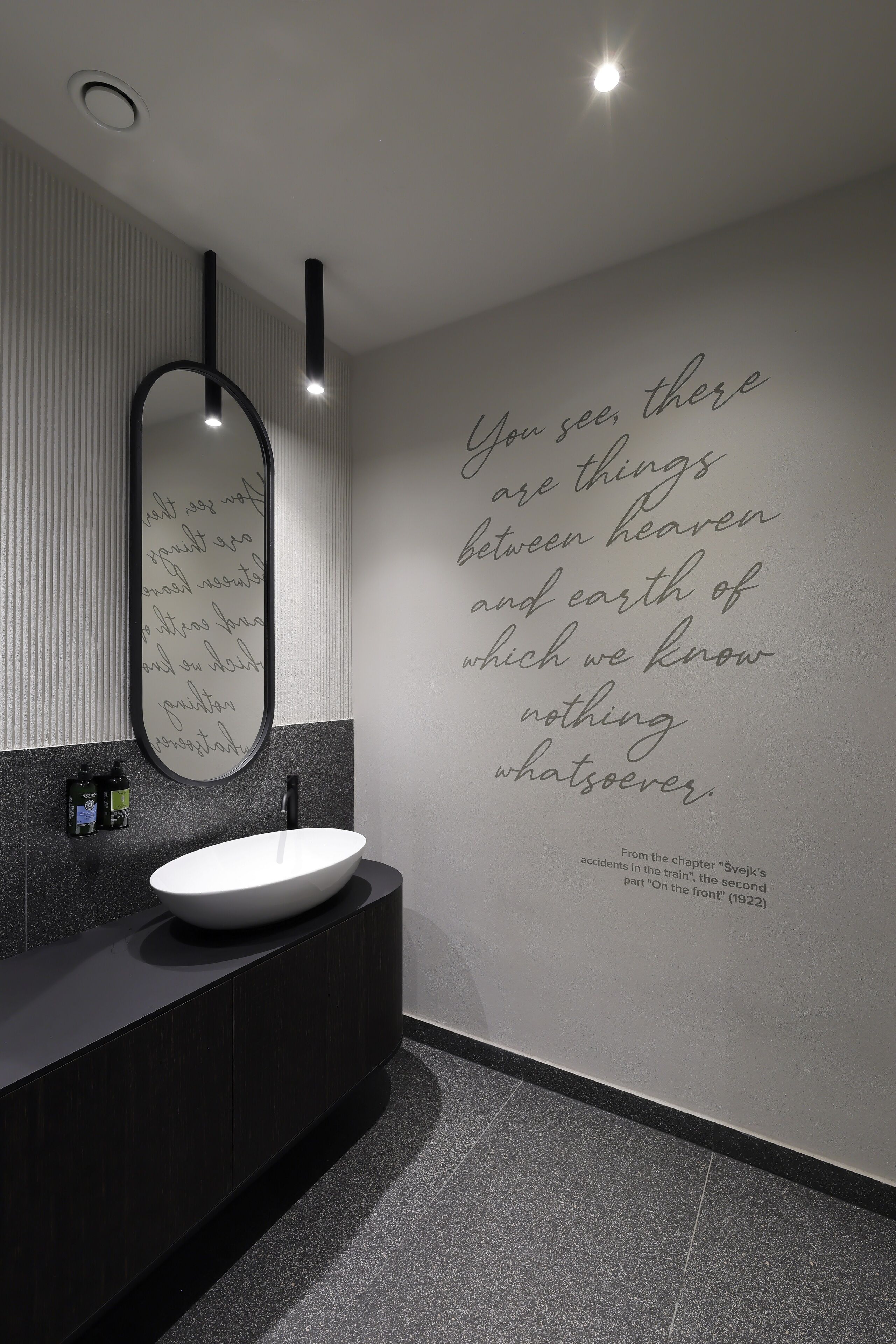 Un baño moderno con un espejo grande, un lavamanos blanco y una cita en la pared.