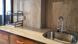 A kitchen with a stainless steel sink, a marble backsplash, and a black wire rack with dishes. - Fancy And Nice Studio At Tamansari The Hive Apartment (Jakarta)