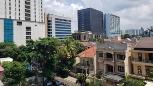 A cityscape with modern buildings, including a high-rise with a blue facade and another with a dark facade. There are residential buildings with red-tiled roofs and balconies. - Fancy And Nice Studio At Tamansari The Hive Apartment (Jakarta)