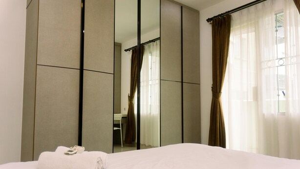 Une chambre d’hôtel avec un grand miroir, un lit soigneusement fait et une vue sur la salle de bain qui se reflète dans le miroir.