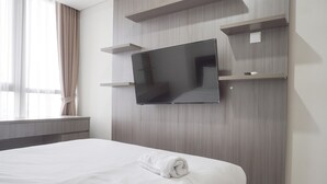 Una habitación de hotel con una cama grande, un televisor de pantalla plana montado en la pared y una ventana con cortinas.