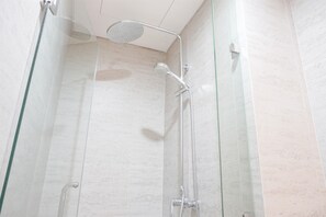 Una ducha moderna con cabina de vidrio, un cabezal de ducha de mano y un grifo empotrado.