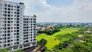 A high-rise building with multiple floors and balconies, overlooking a green park and residential area. - Nice And Comfy 1Br At Casa De Parco Apartment (Pagedangan)