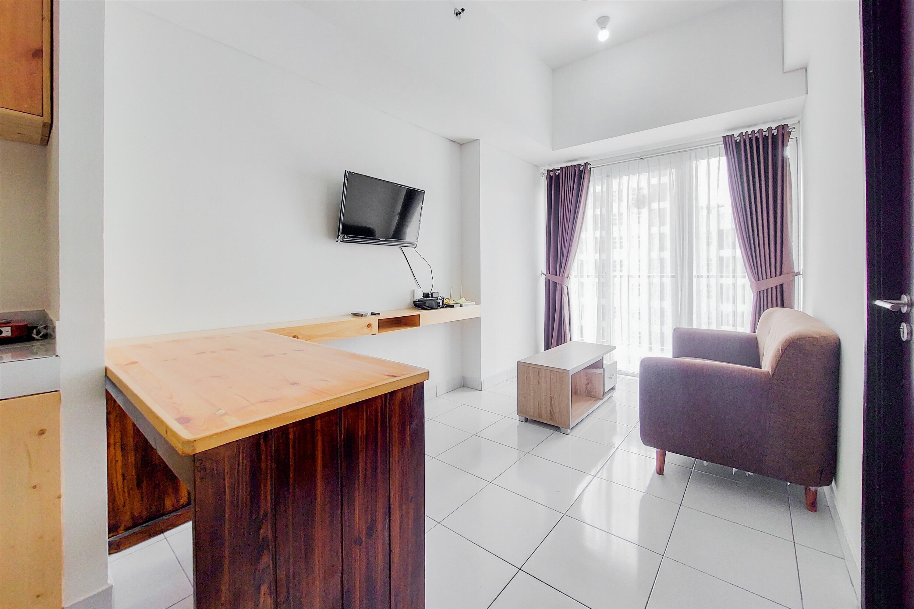 Quarto moderno com escrivaninha de madeira, televisão na parede, poltrona estofada e janela com cortinas.