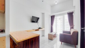 A modern room with a wooden desk, a television mounted on the wall, a cushioned chair, and a window with curtains. - Nice And Comfy 1Br At Casa De Parco Apartment (Pagedangan)