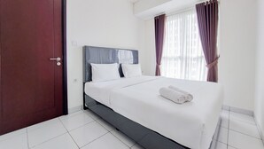 A hotel room with a large bed, a wooden door, and a window with curtains. - Nice And Comfy 1Br At Casa De Parco Apartment (Pagedangan)