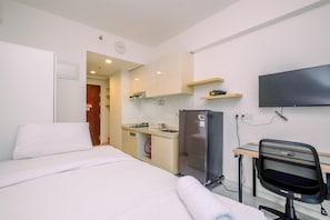 A hotel room with a bed, a desk with a chair, a refrigerator, a television, and a kitchenette. - Modern Look And Comfy Studio At Sky House Bsd Apartment (Pagedangan)