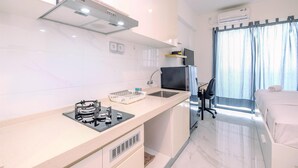 A compact hotel room with a kitchenette, a bed, a desk, and a window with curtains.