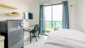 A hotel room with a bed, desk, chair, refrigerator, TV, air conditioning unit, and a window with curtains.