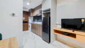 A compact kitchen with a built-in washing machine, a black refrigerator, and a TV on a wooden shelf. - Gorgeous 1Br Apartment At The Smith Alam Sutera (Tangerang)